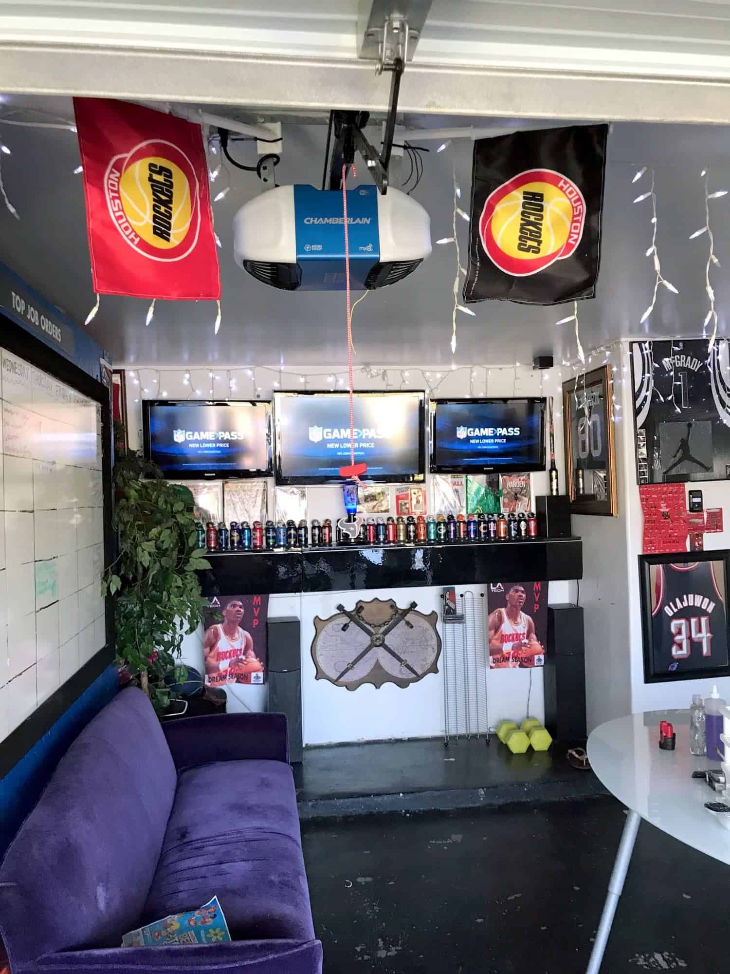 Three TVs mounted side by side in a home man cave with Houston Rockets flags and sports memorabilia