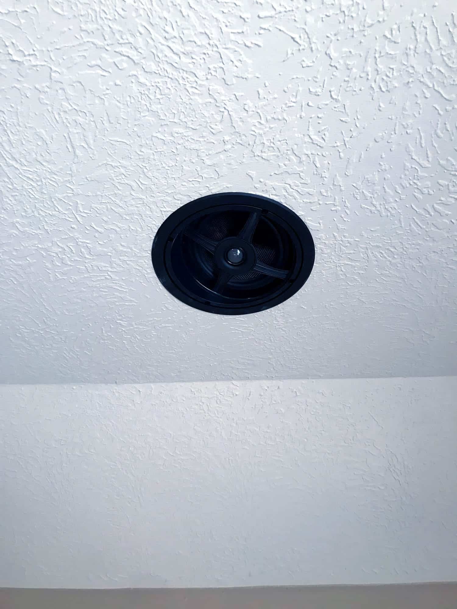 Close-up of a round in-ceiling surround-sound speaker installed in a textured ceiling