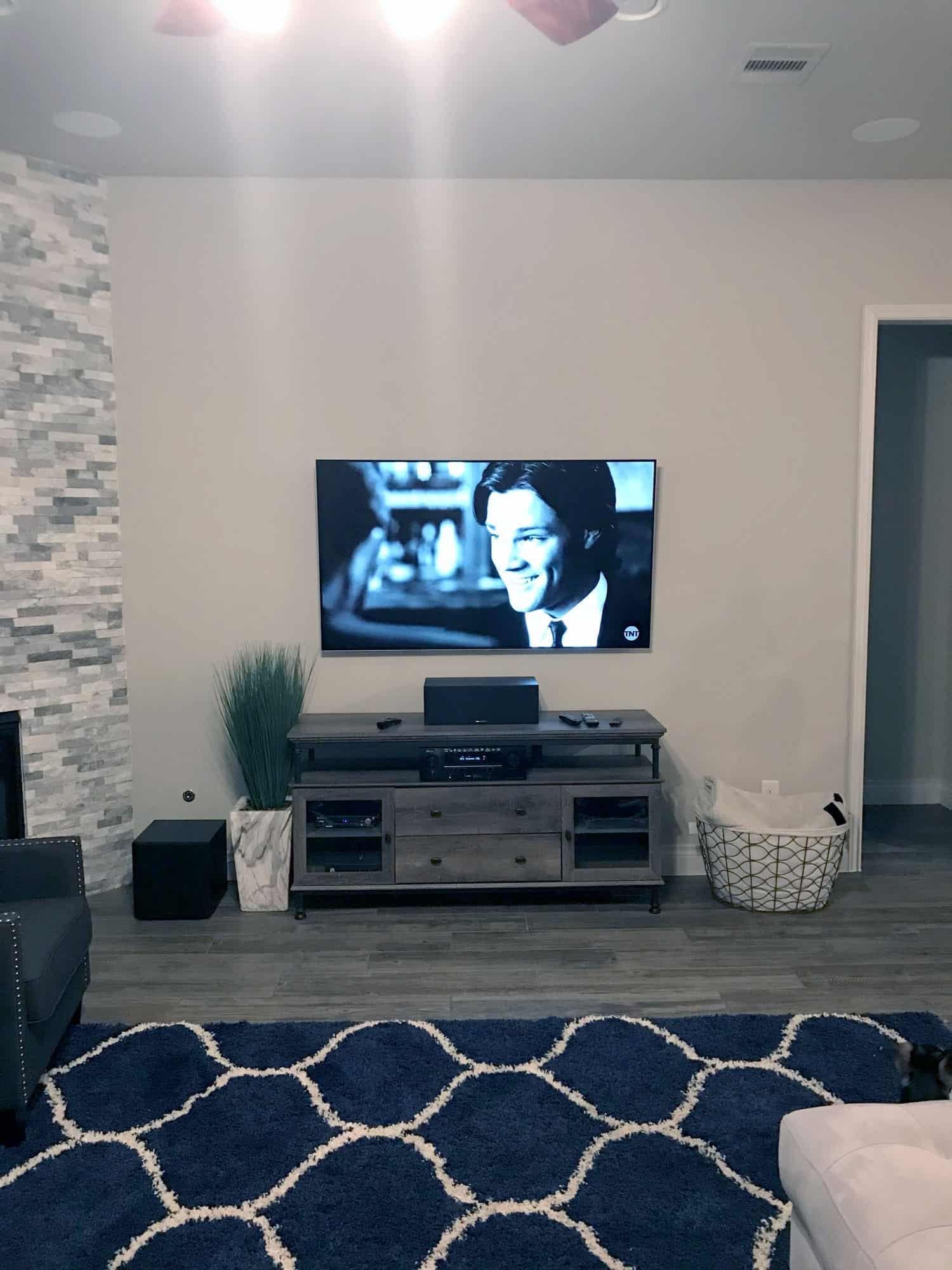 TV mounted above a wood media console with AV components and a blue patterned area rug