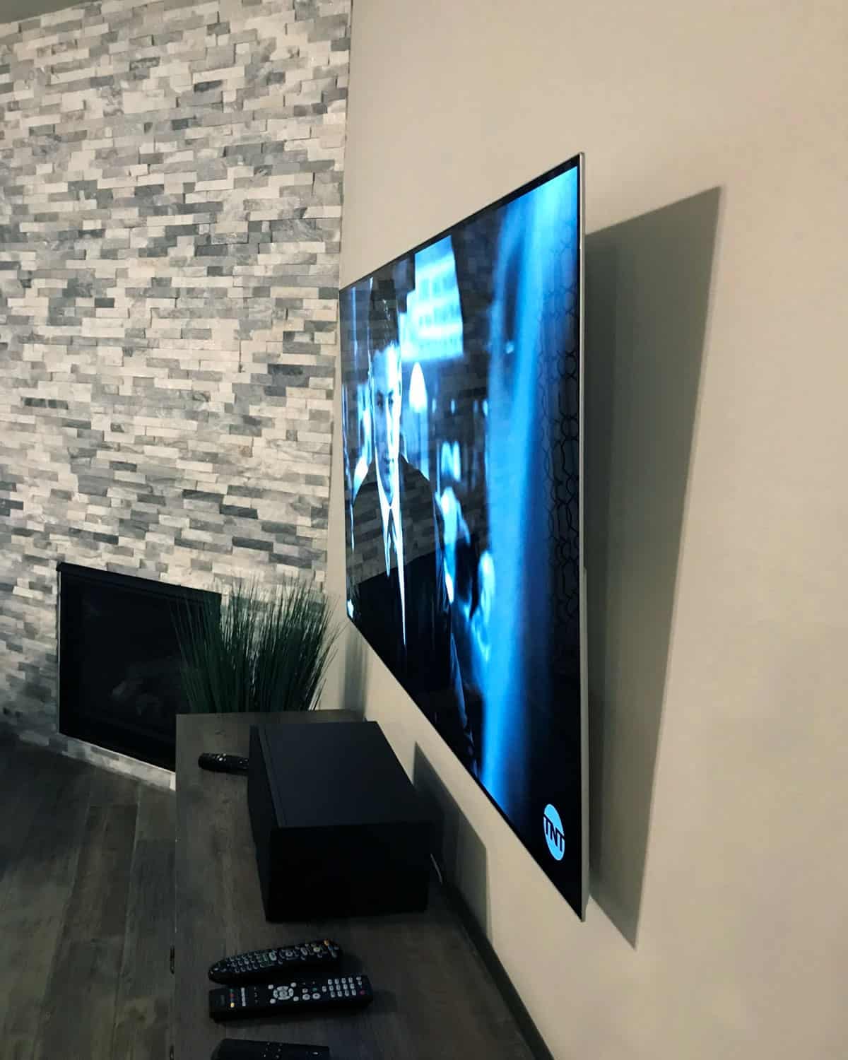 Wide view of a TV mounted beside a stacked-stone fireplace wall showing a TNT drama