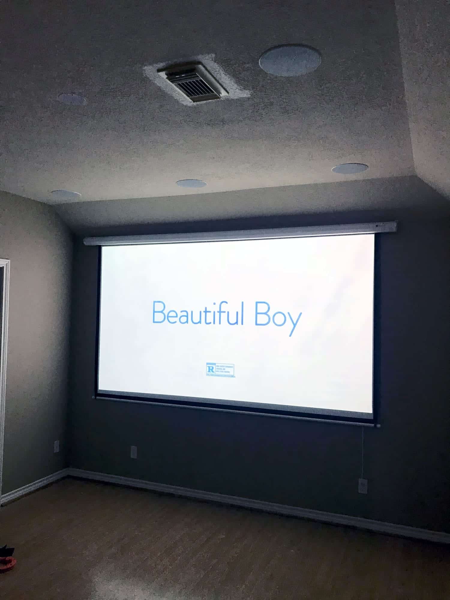 Motorized projector screen lowered in a home theater, displaying a movie title card