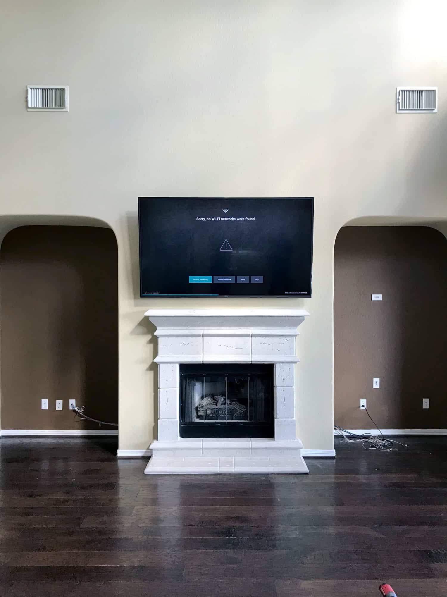 Wide view of a TV mounted above a white stone fireplace between two archways during setup