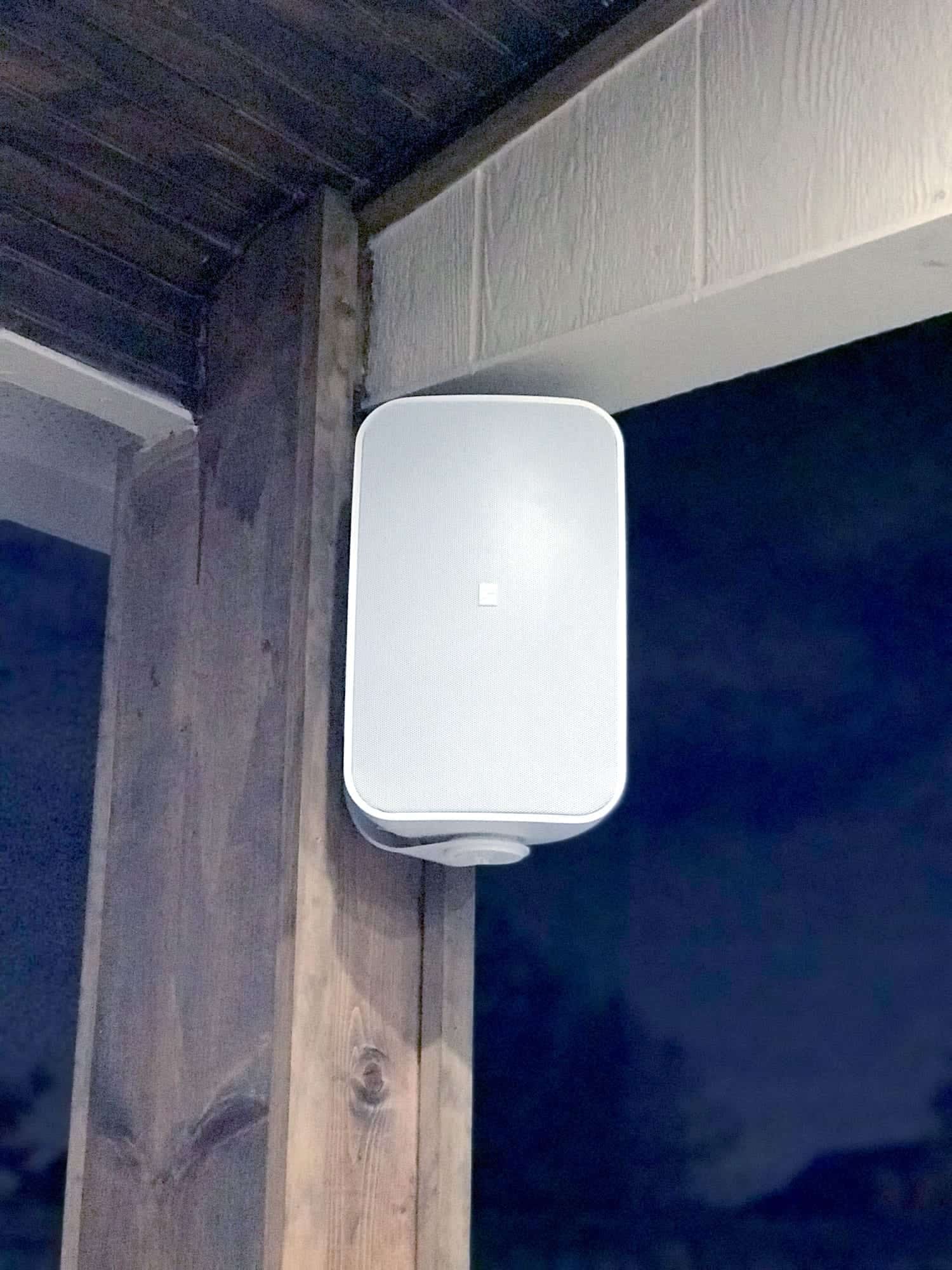 Close-up of a white outdoor-rated speaker mounted in the corner of a covered patio ceiling
