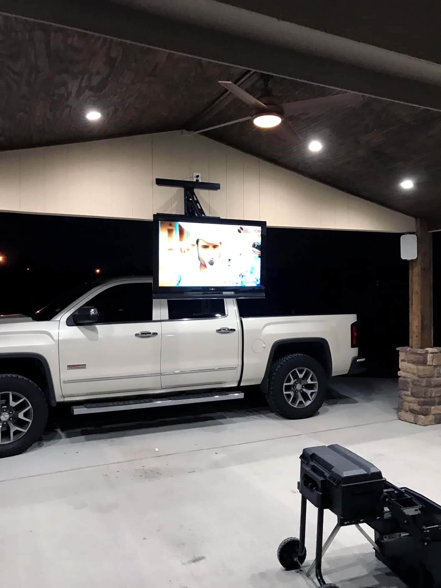 TV on a motorized ceiling lift retracted above a pickup truck under a covered outdoor patio