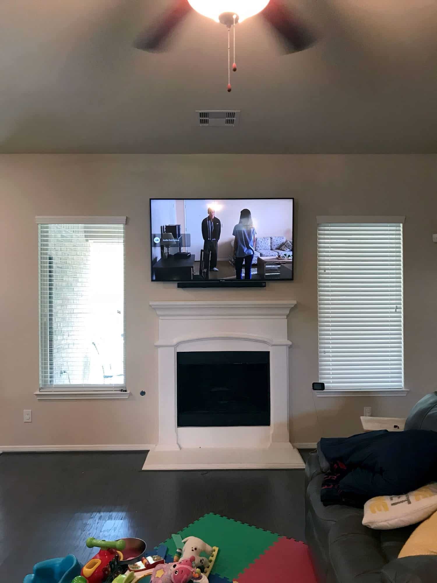 TV mounted above a white fireplace mantel in a family room with children's toys on the floor