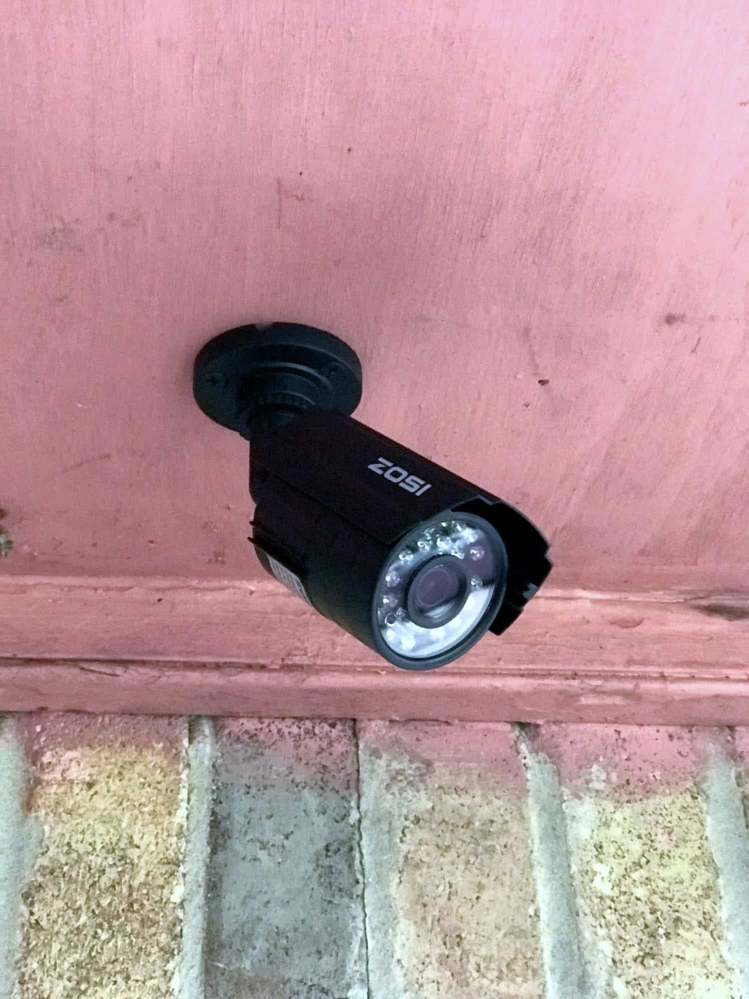 Close-up of a black bullet security camera mounted under a covered porch eave