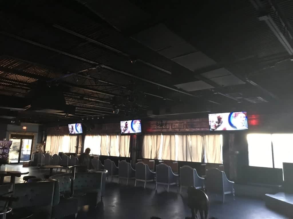 Three TVs mounted in a row above curtained windows in a restaurant or bar dining area