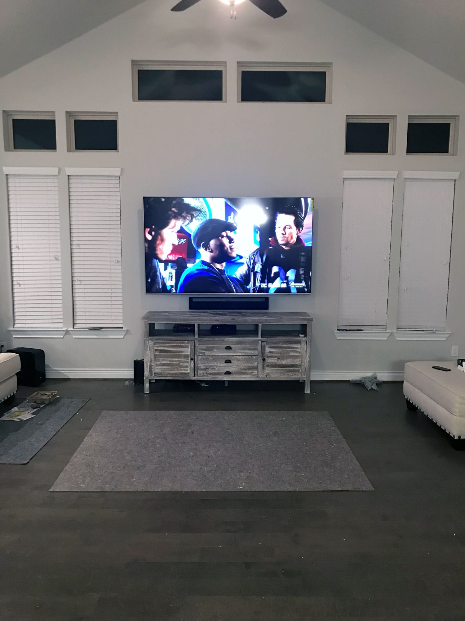 TV mounted on a wall above a rustic wood console, showing a movie scene in a vaulted-ceiling living room