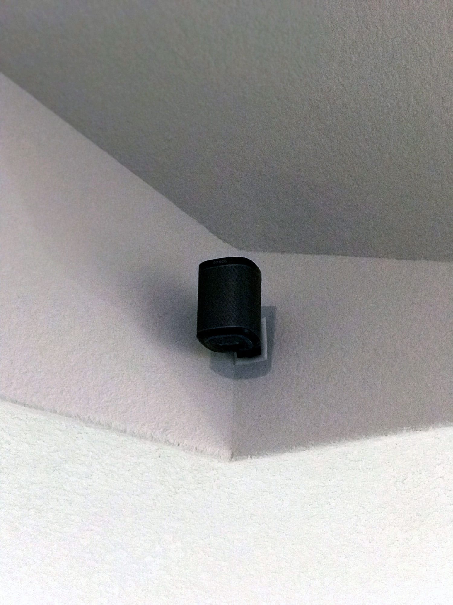 Close-up of a black Sonos wireless speaker mounted on a ceiling corner bracket