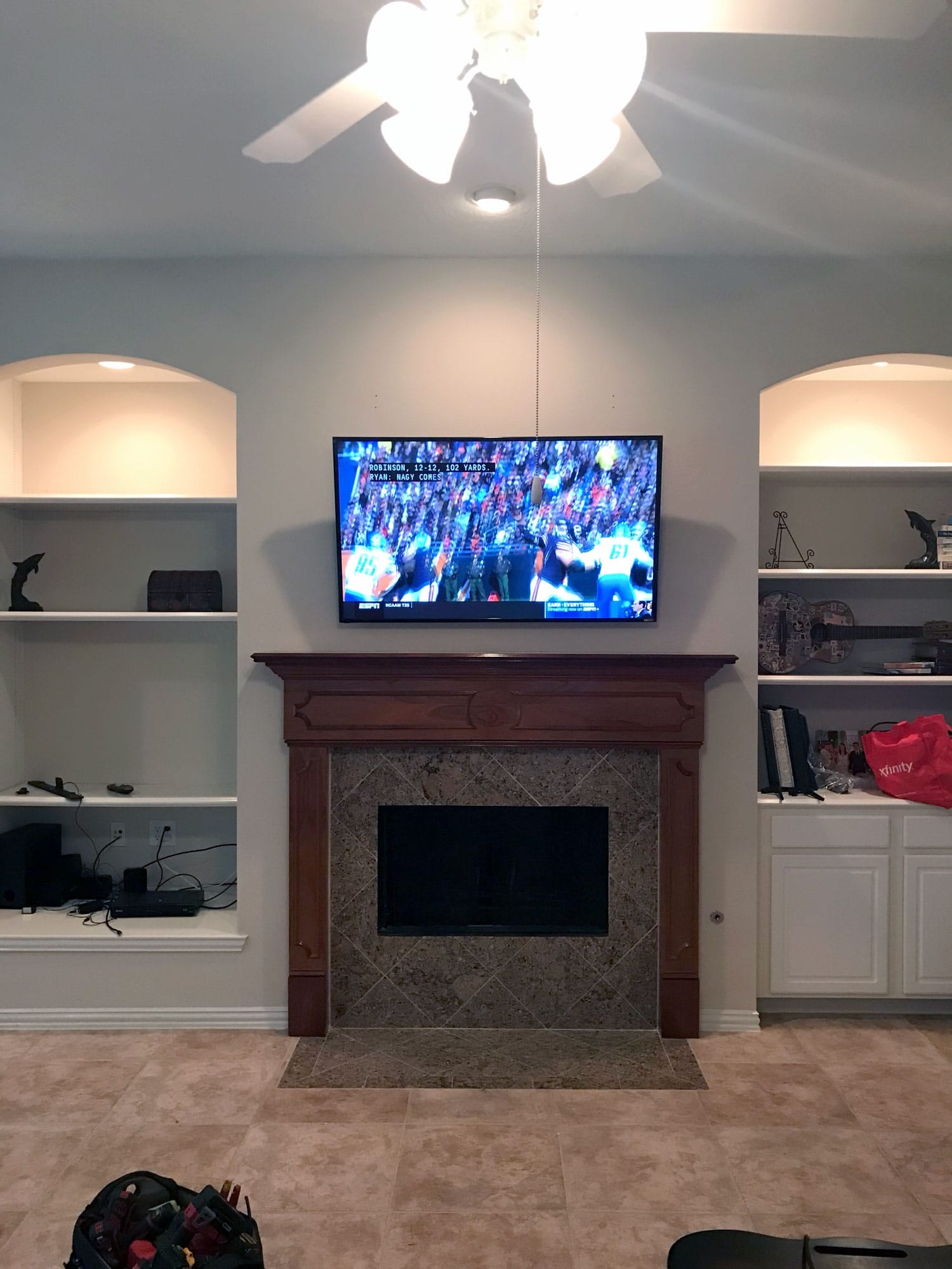 TV mounted above a dark wood fireplace mantel showing an ESPN football broadcast, flanked by built-in shelving