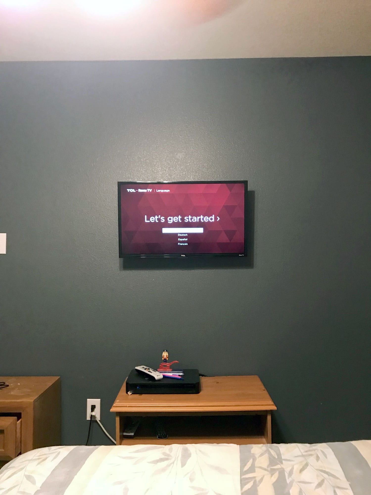 TV mounted on a dark accent wall showing the Roku TV setup screen in a bedroom