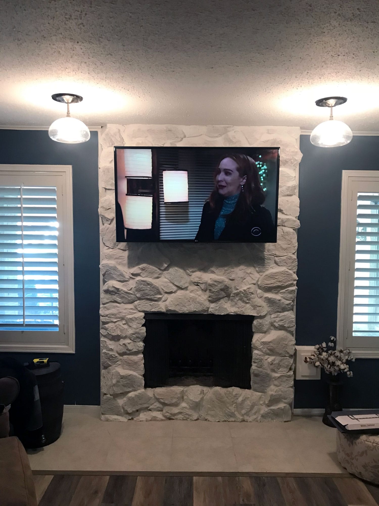 TV mounted above a stone fireplace flanked by pendant lights in a room with dark blue accent walls
