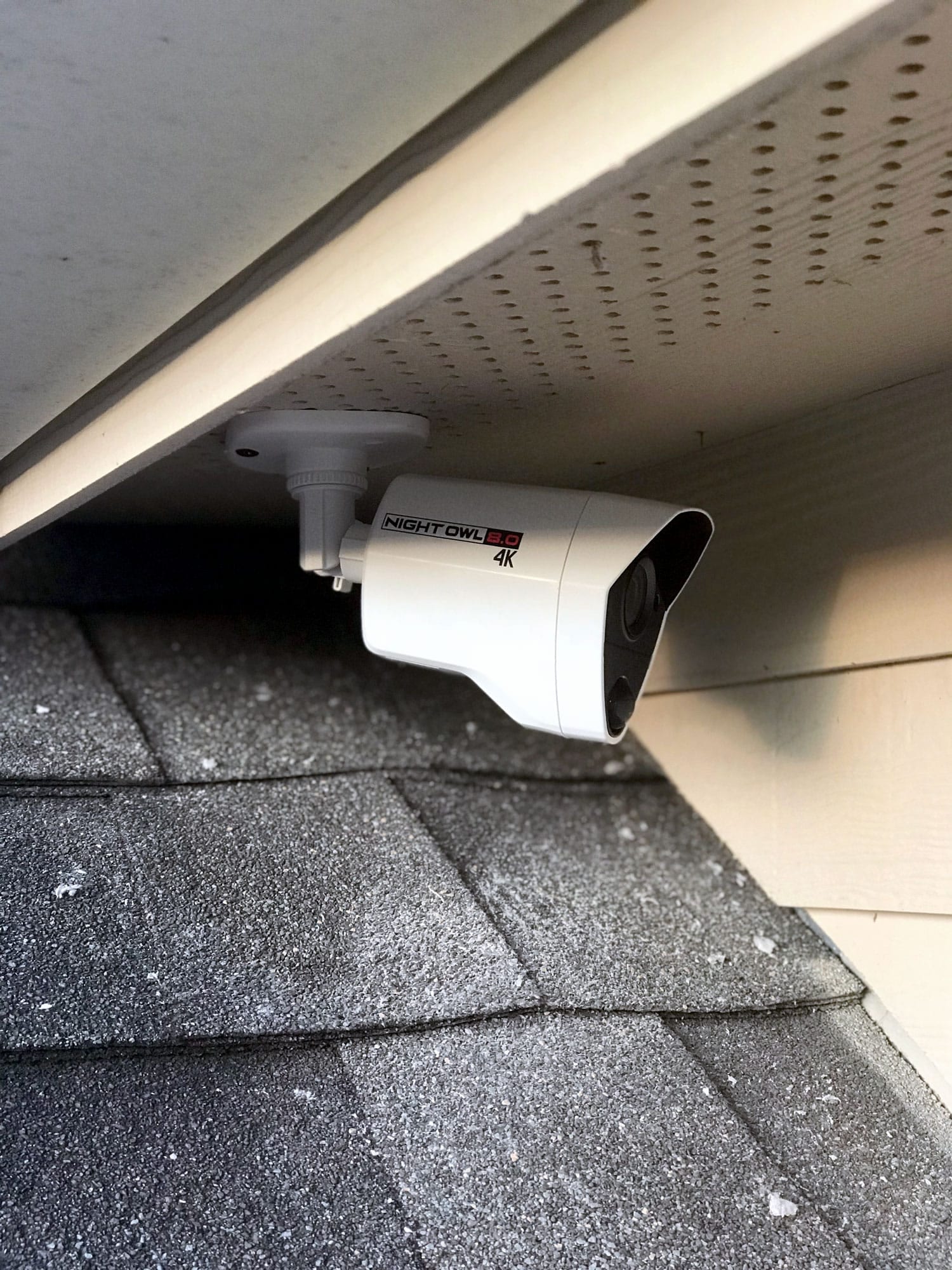 Close-up of a white outdoor security camera mounted under a roof eave on a brick home