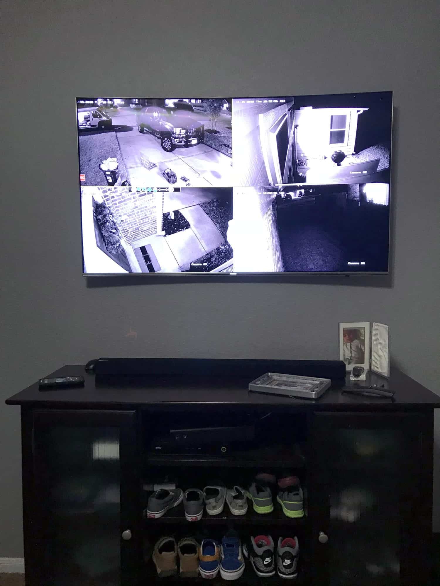 Four-camera security monitor mounted above a dark wood media cabinet showing night-vision footage