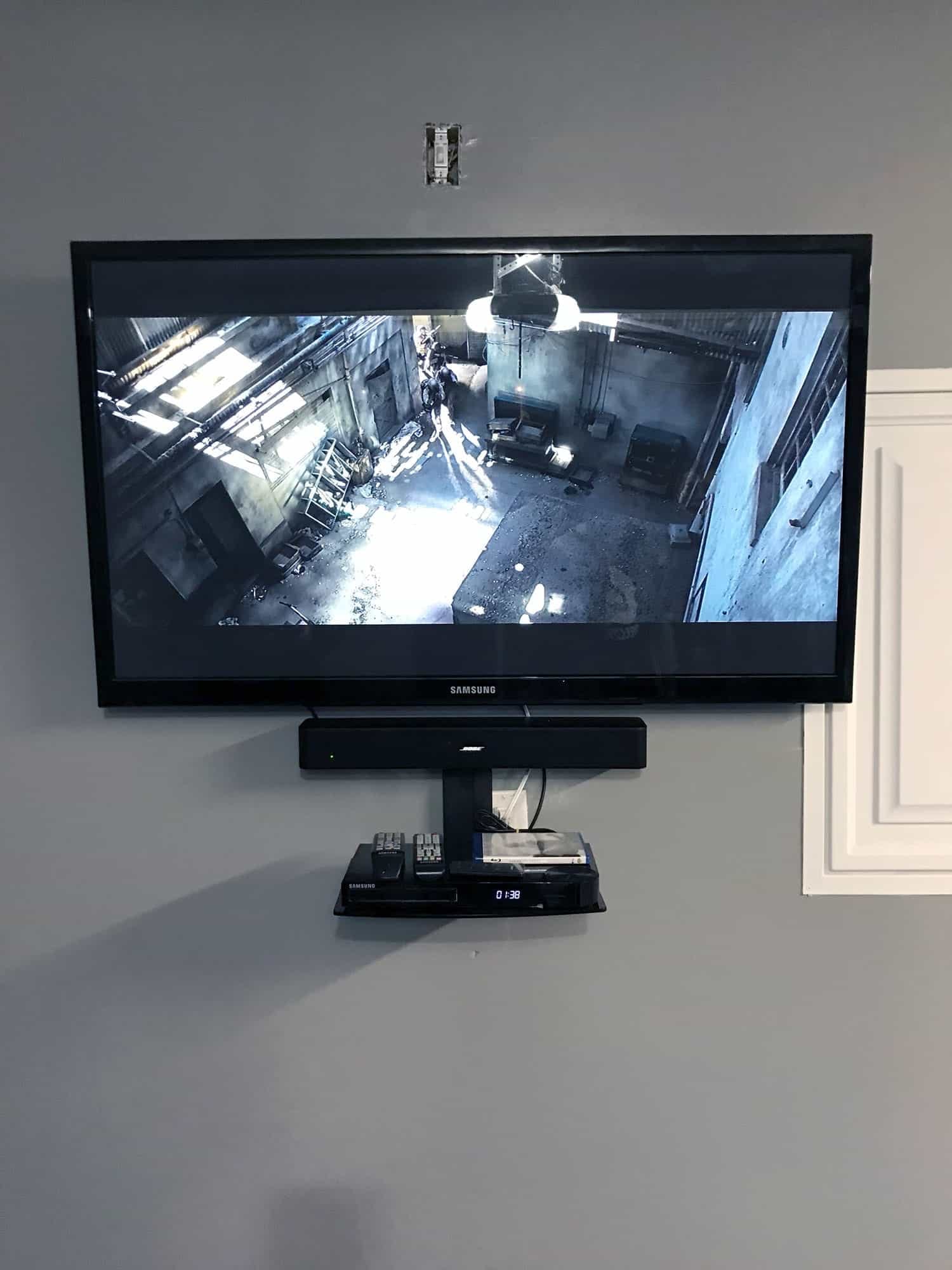 TV mounted on a wall with a soundbar and AV equipment below, showing a video game scene