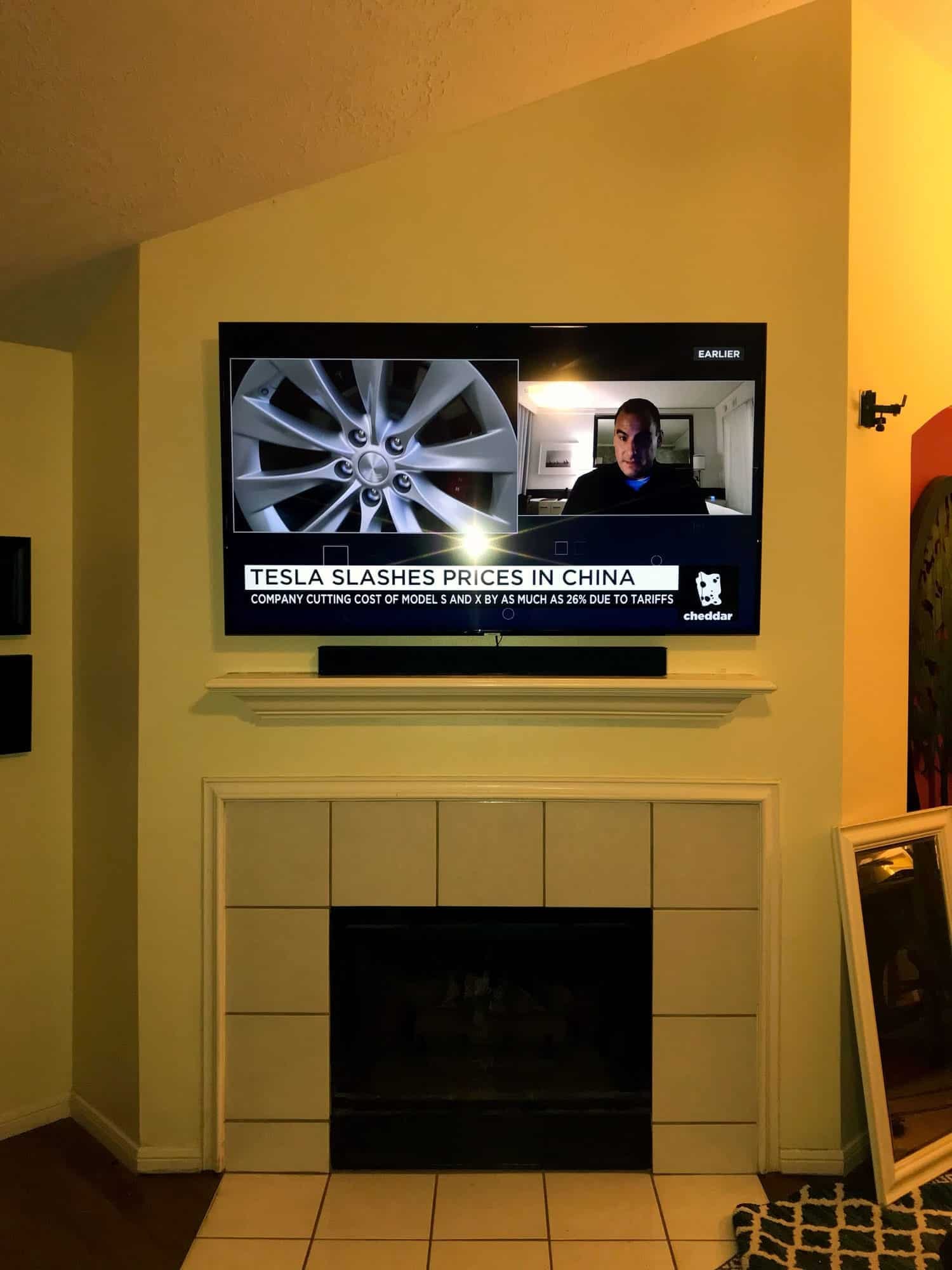 TV mounted above a white tiled fireplace showing a video call and news broadcast split-screen