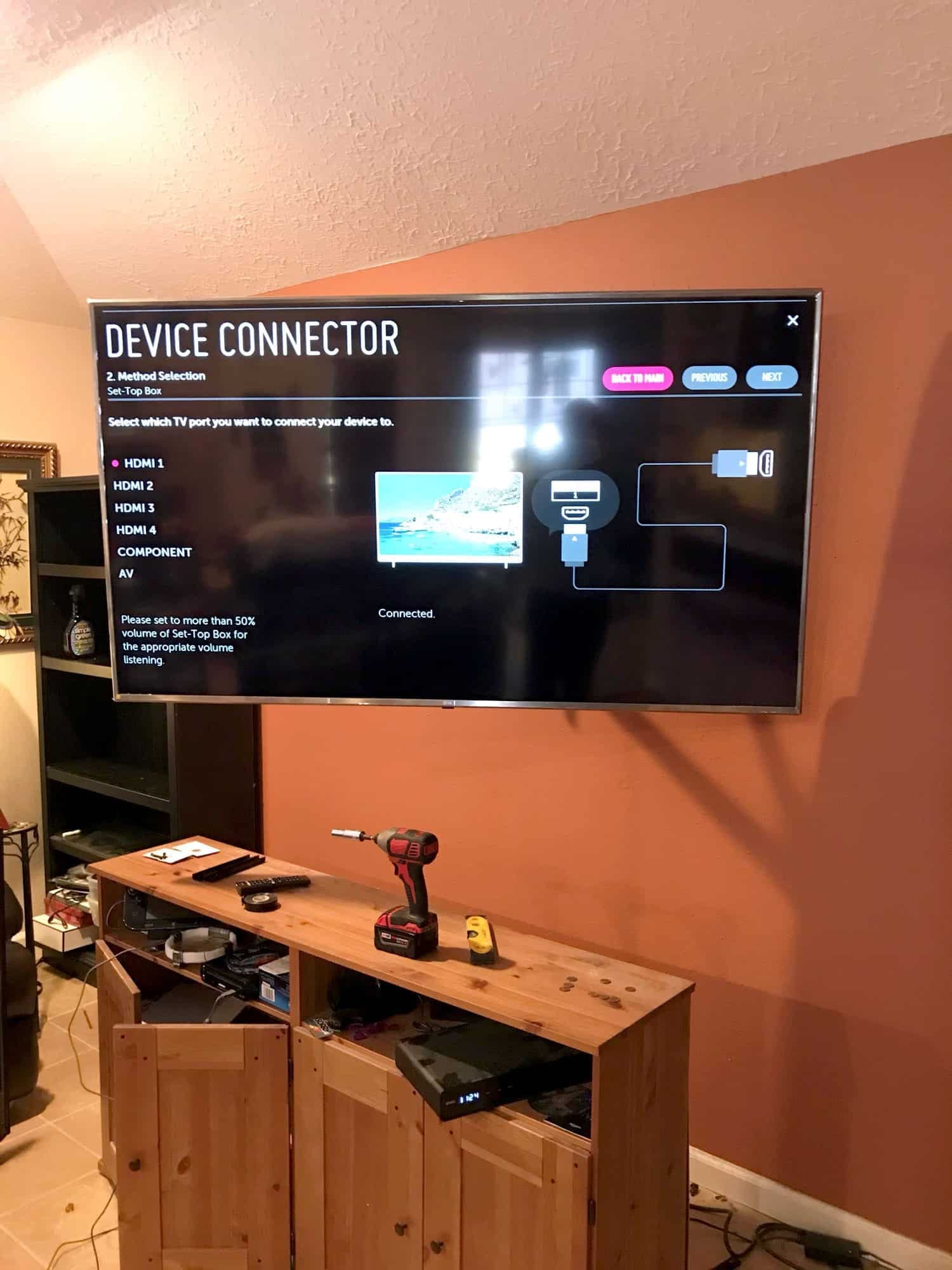 TV mounted on an orange accent wall showing an HDMI device connection setup screen