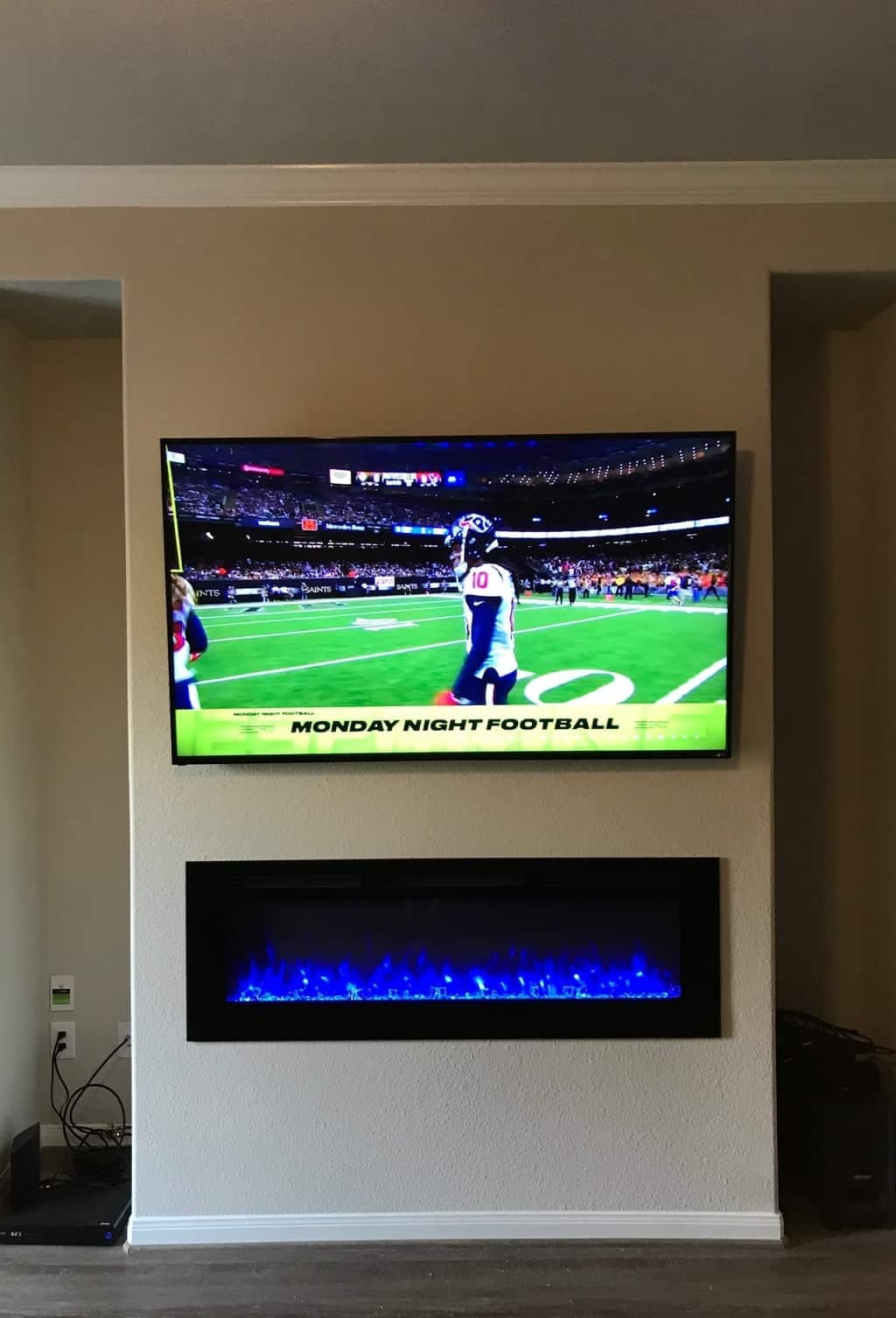 TV mounted above a black built-in electric fireplace with blue flame lighting, showing Monday Night Football