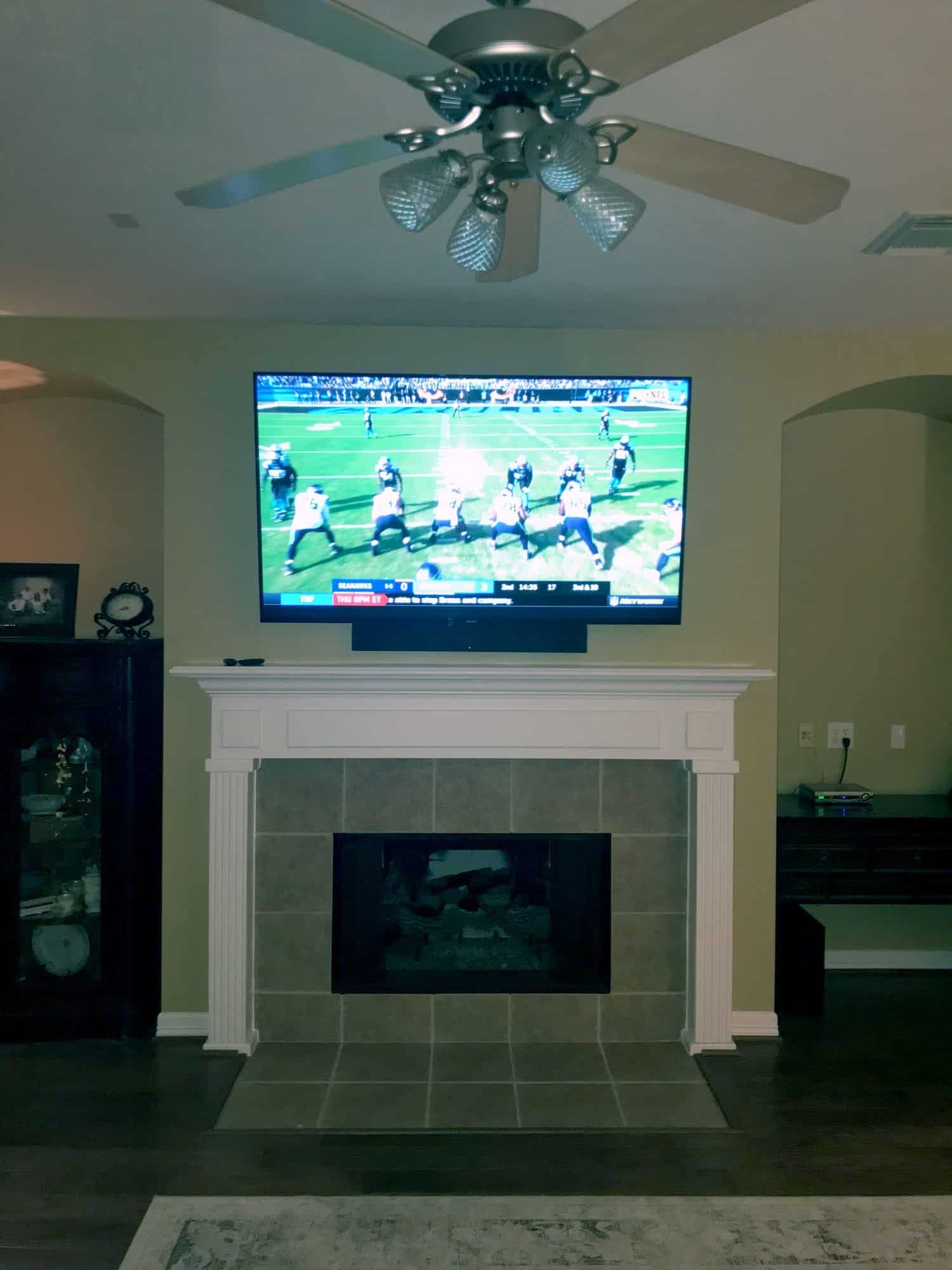 TV mounted above a white fireplace mantel showing an NFL broadcast in an elegant living room