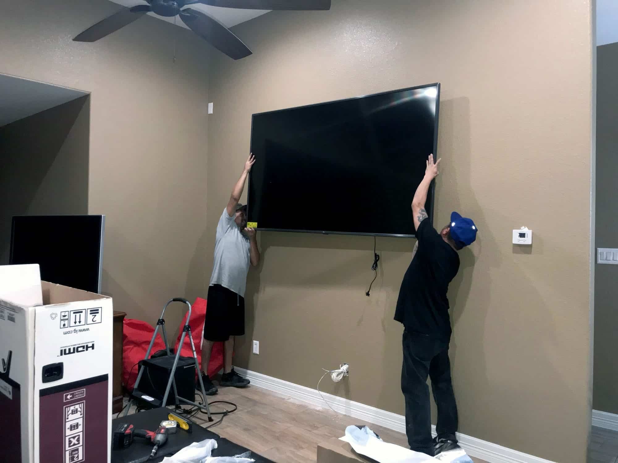 Two installers lifting a large flat-screen TV onto a wall mount together