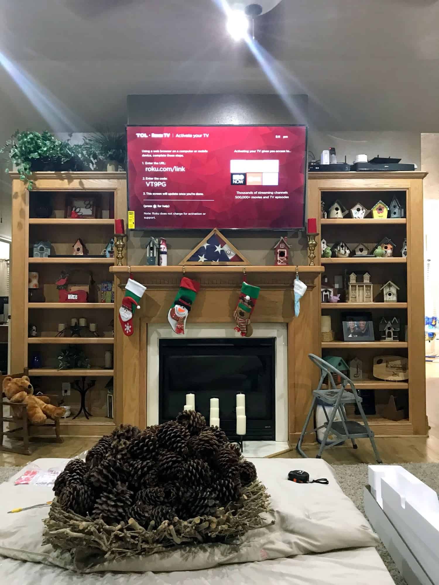 TV mounted above a wood fireplace mantel between built-in bookshelves filled with birdhouse collectibles