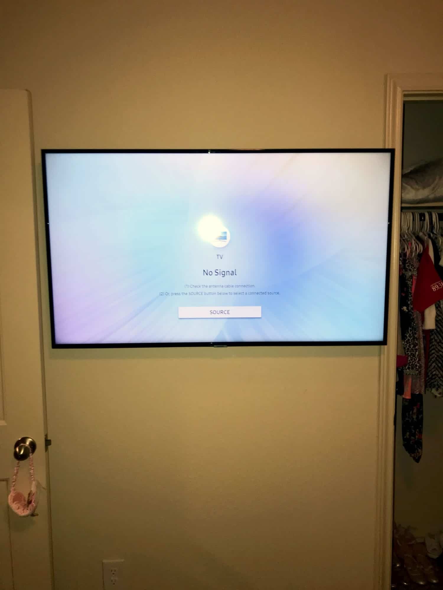 TV mounted on a wall showing a no-signal screen near a bedroom closet