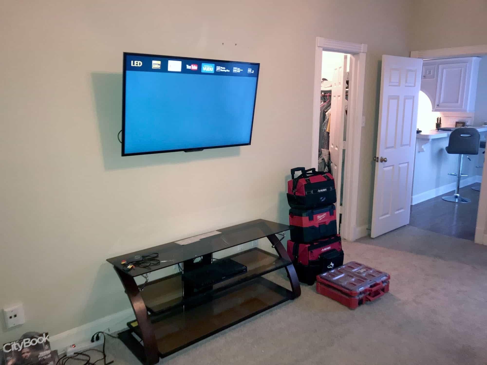 TV mounted on a wall displaying a streaming app menu, with moving bags and tool cases on the floor