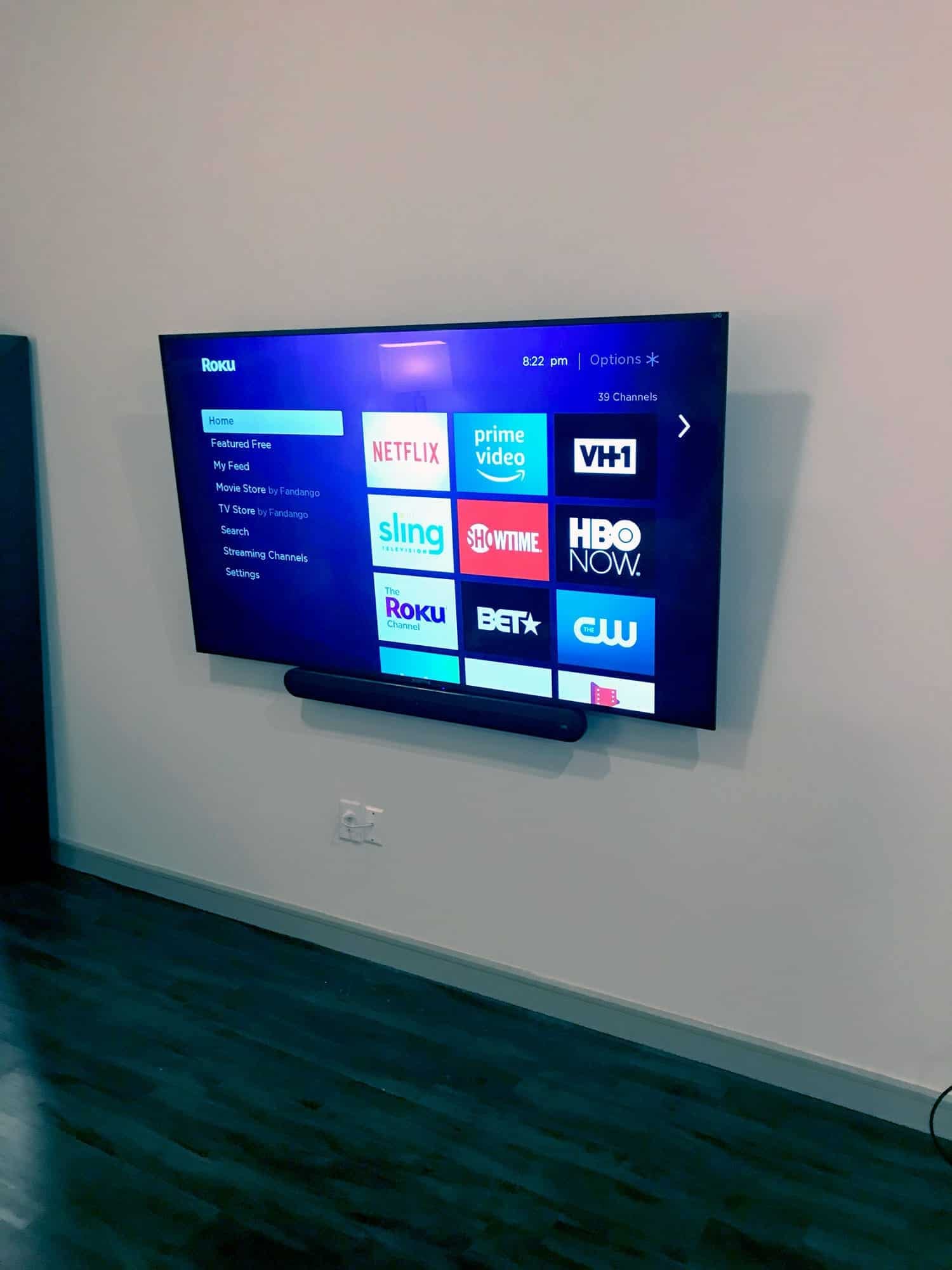 Wall-mounted TV with a soundbar underneath showing a streaming home screen
