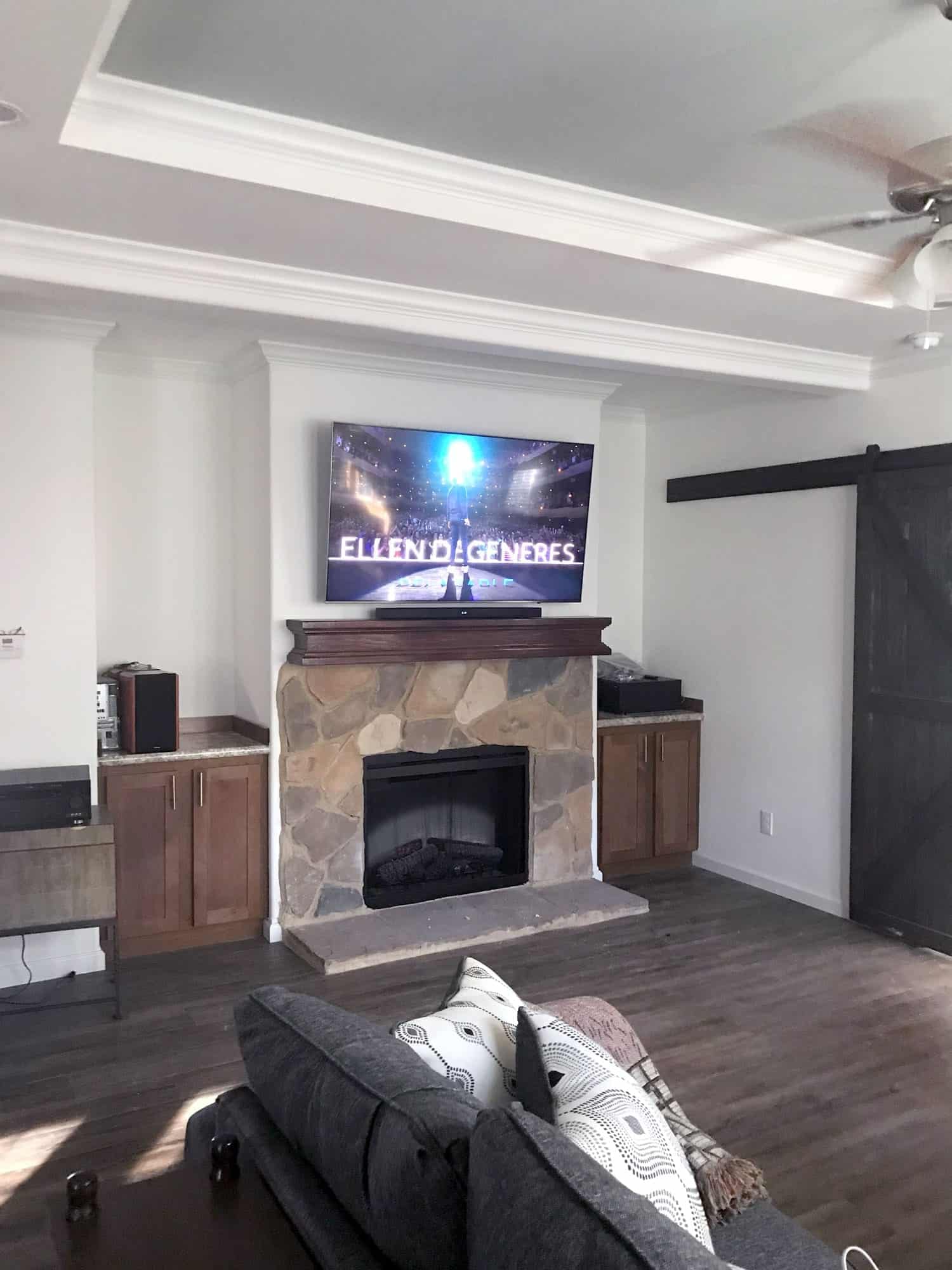 TV mounted above a stone fireplace showing a talk show, next to a black sliding barn door