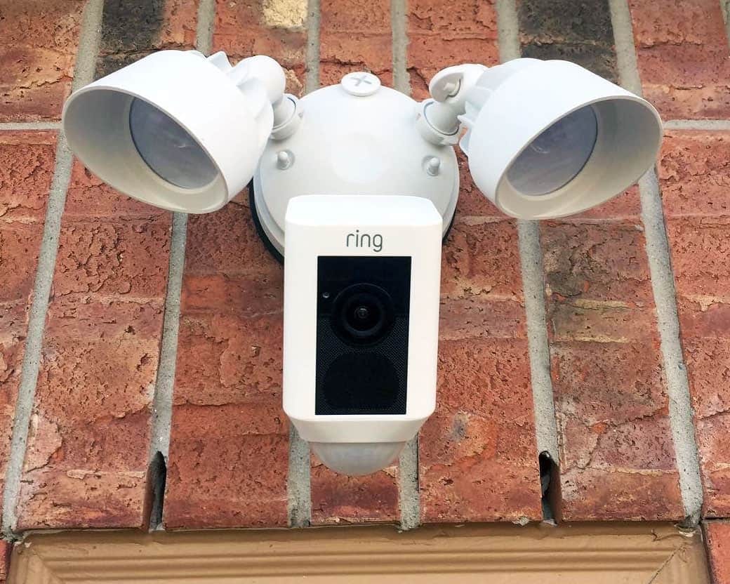 Close-up of a white Ring floodlight security camera mounted on a brick exterior wall
