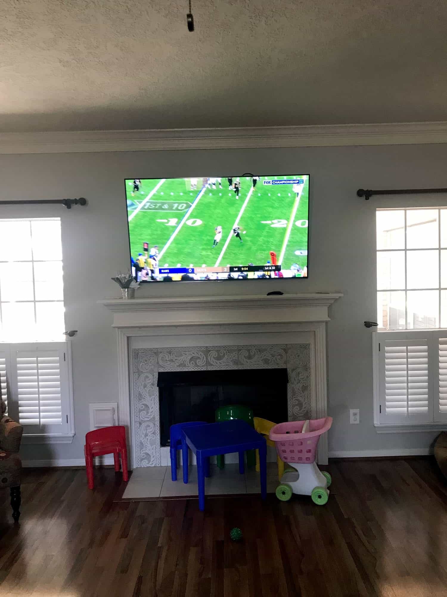 TV mounted above a white fireplace mantel showing a football broadcast, with children's furniture on the hearth below