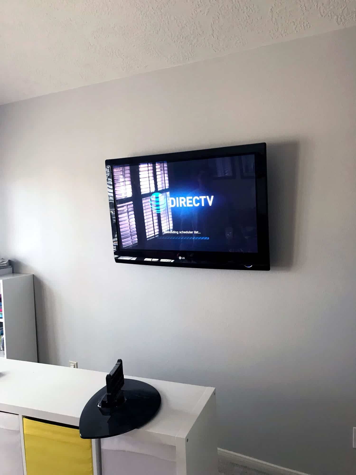 TV mounted on a wall displaying a DIRECTV setup screen above a white media stand