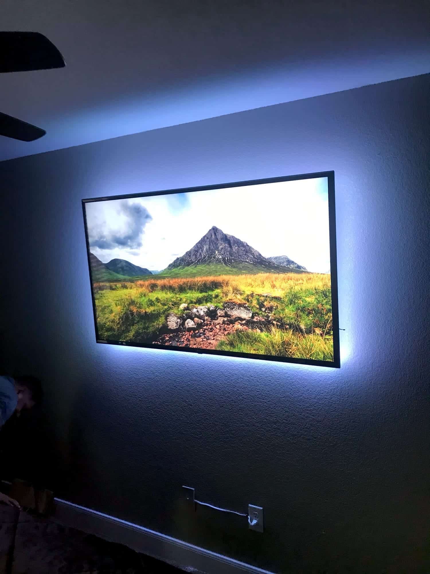 Wall-mounted TV with blue LED backlighting displaying a mountain and valley landscape