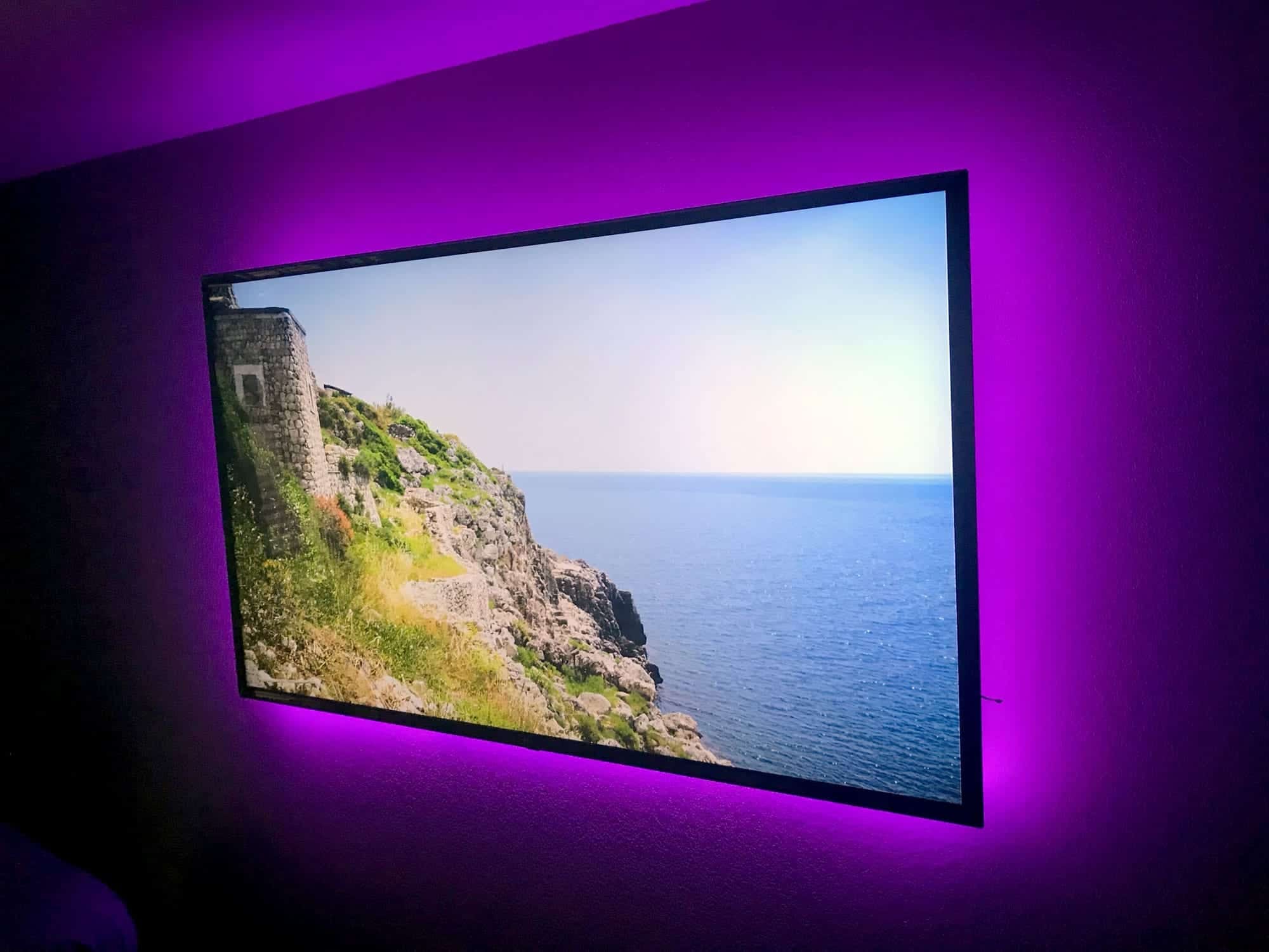 Wall-mounted TV with purple LED backlighting displaying a coastal cliff and ocean scene