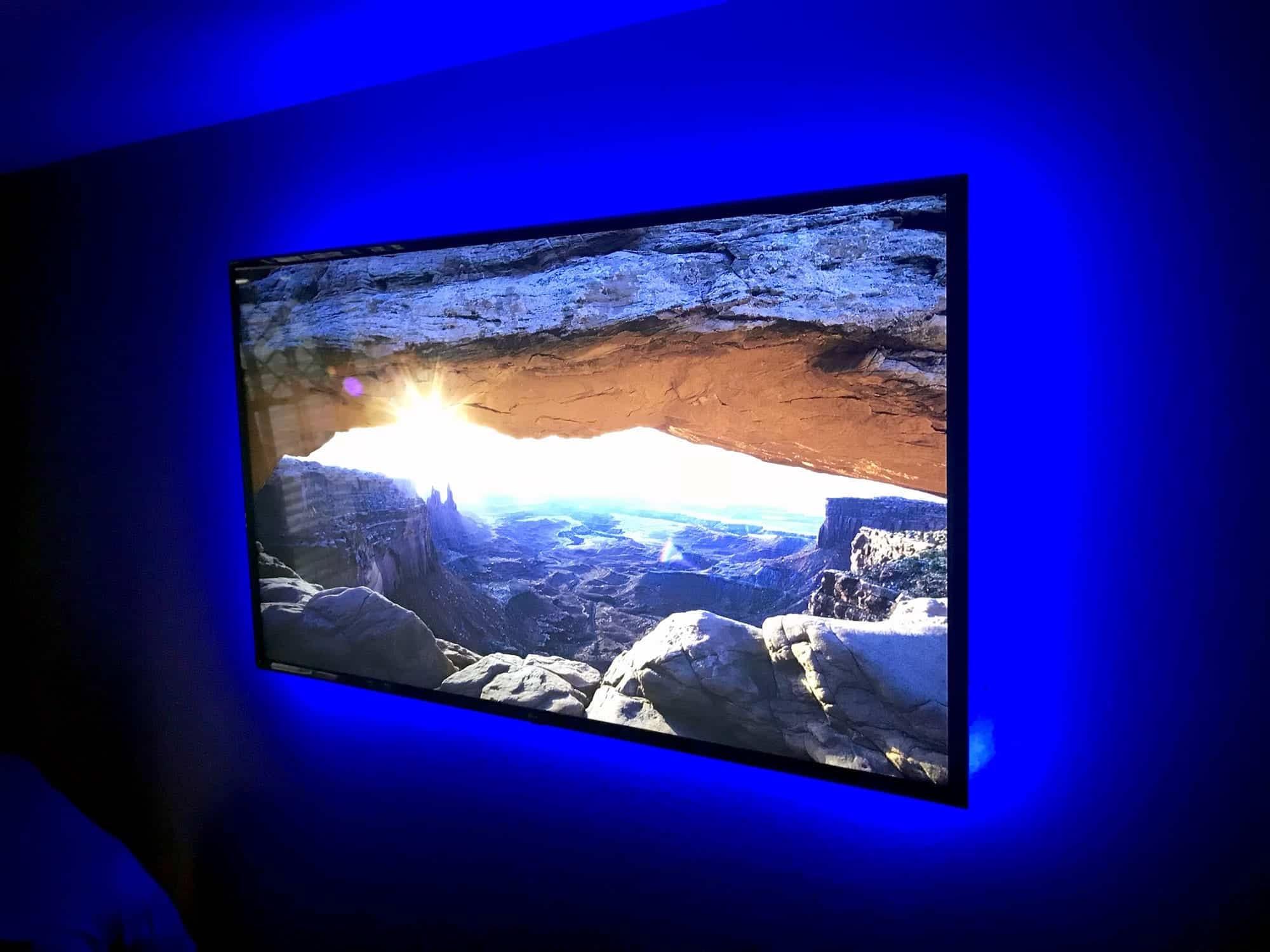 Wall-mounted TV with blue LED backlighting displaying a desert canyon landscape