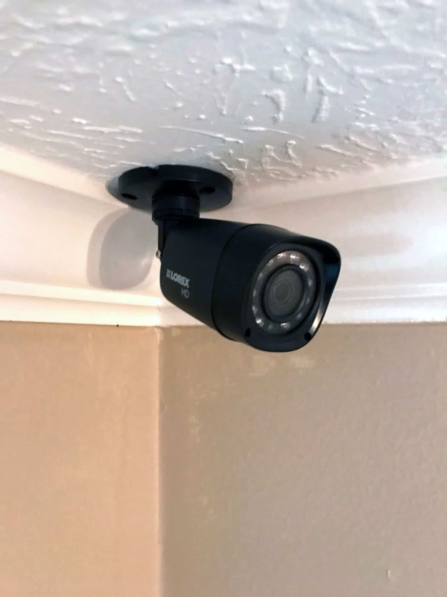 Close-up of a black indoor security camera mounted in a ceiling corner