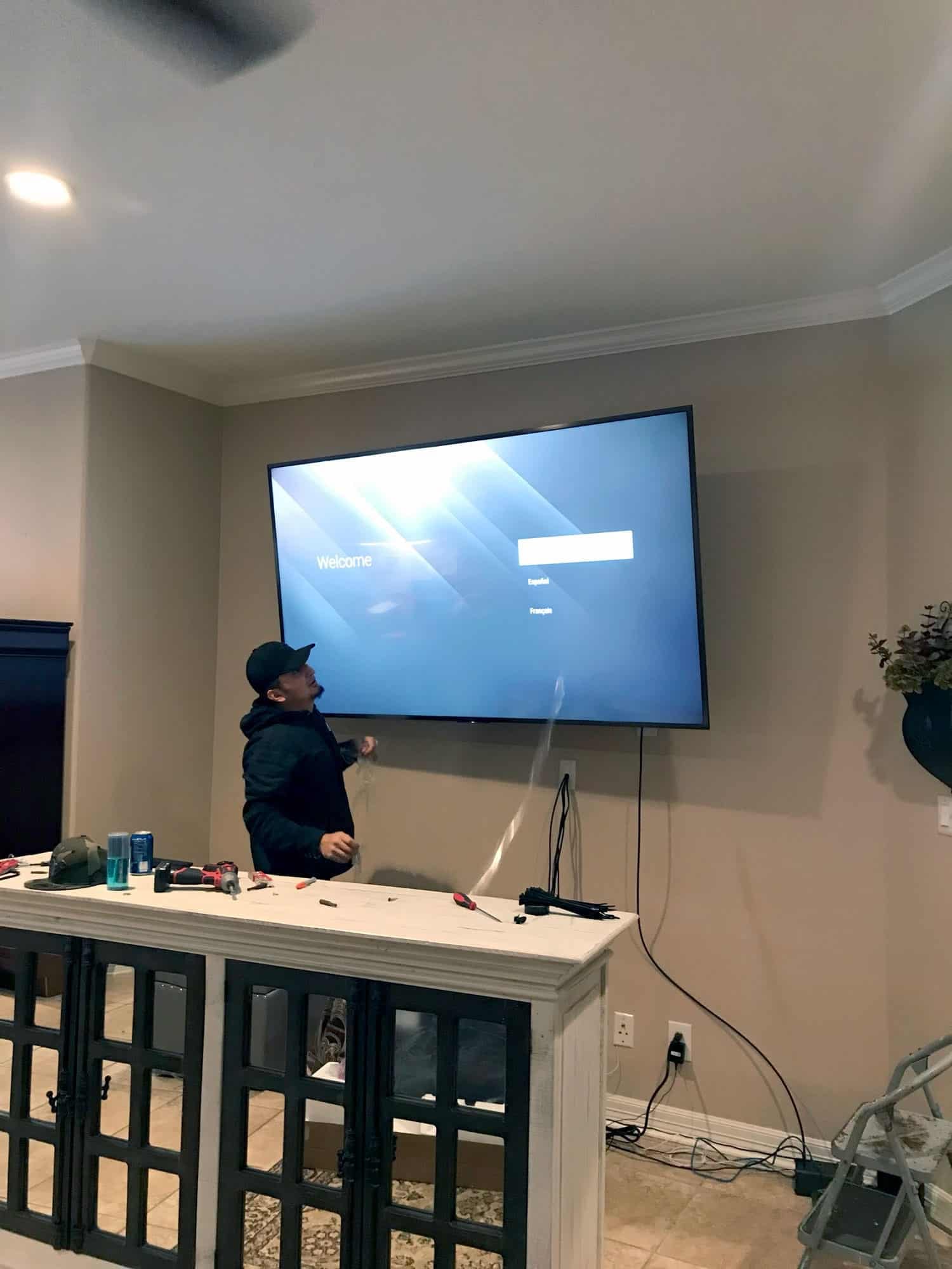 Installer setting up a newly mounted TV displaying a language selection welcome screen