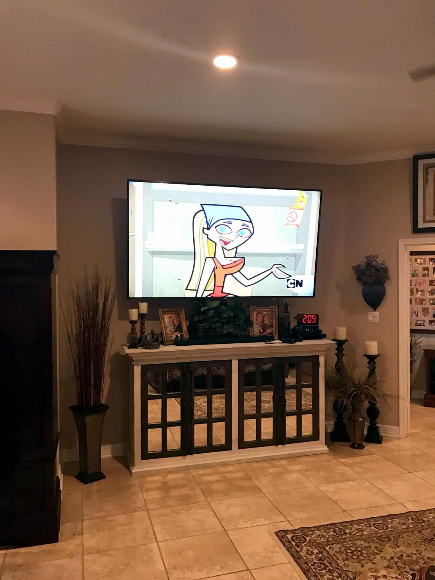 TV mounted above a mirrored console table showing a cartoon, with candles on either side
