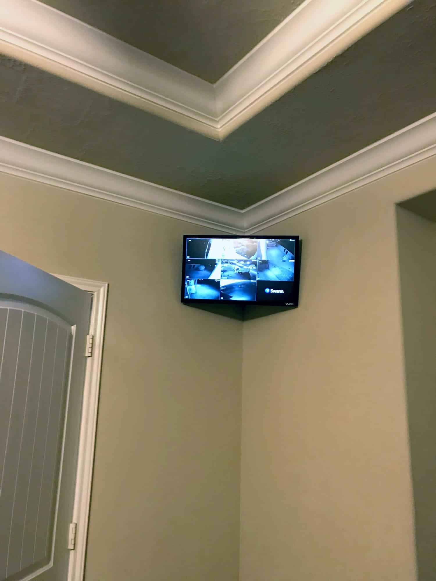 Small security monitor mounted in a ceiling corner showing an eight-camera grid in a vaulted entryway