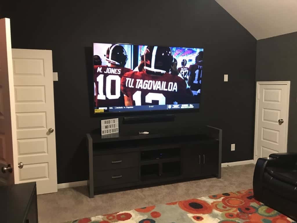 TV mounted on a black accent wall showing a college football broadcast in a media room