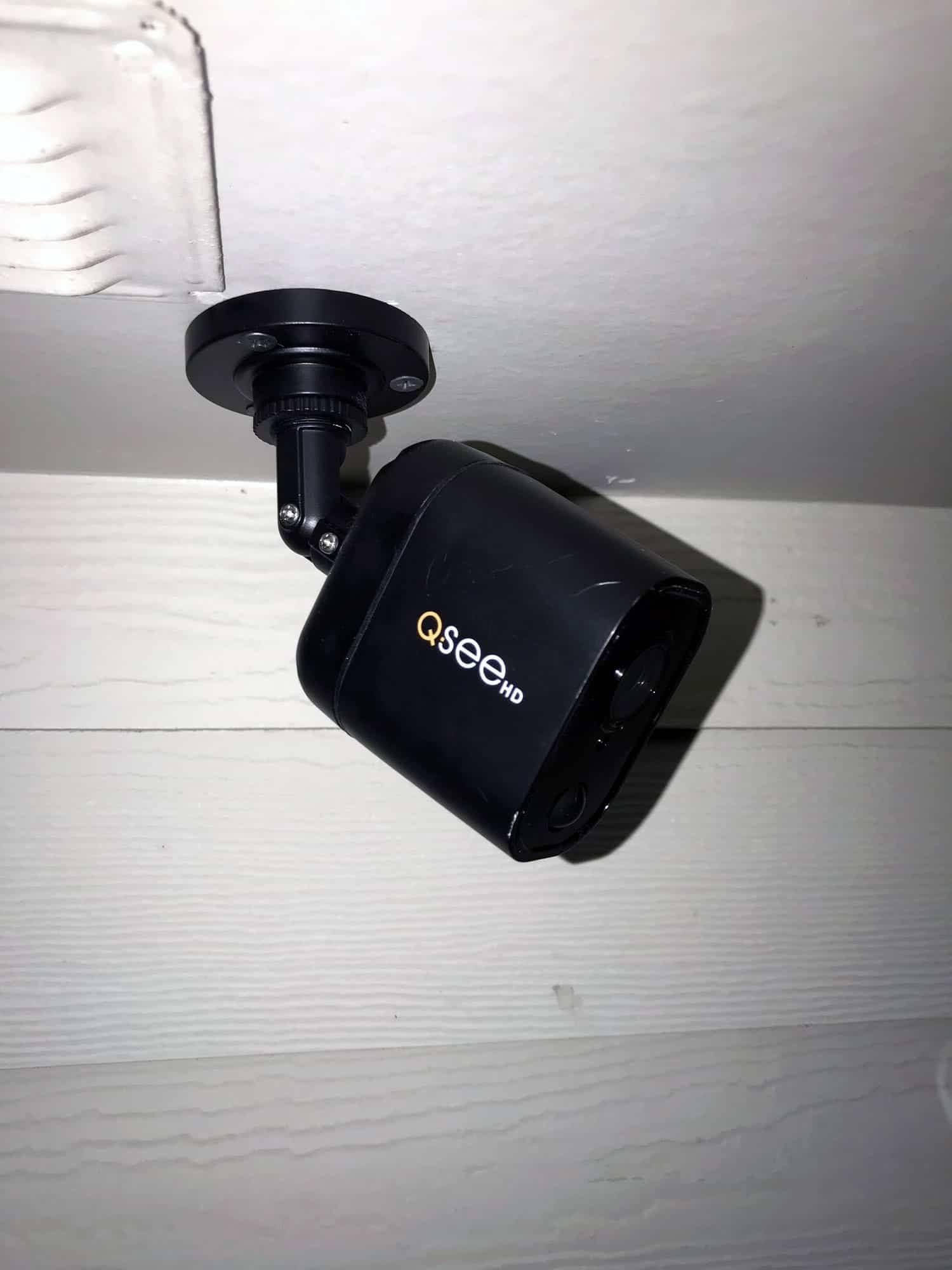 Black bullet-style security camera mounted under a roof eave overlooking a backyard
