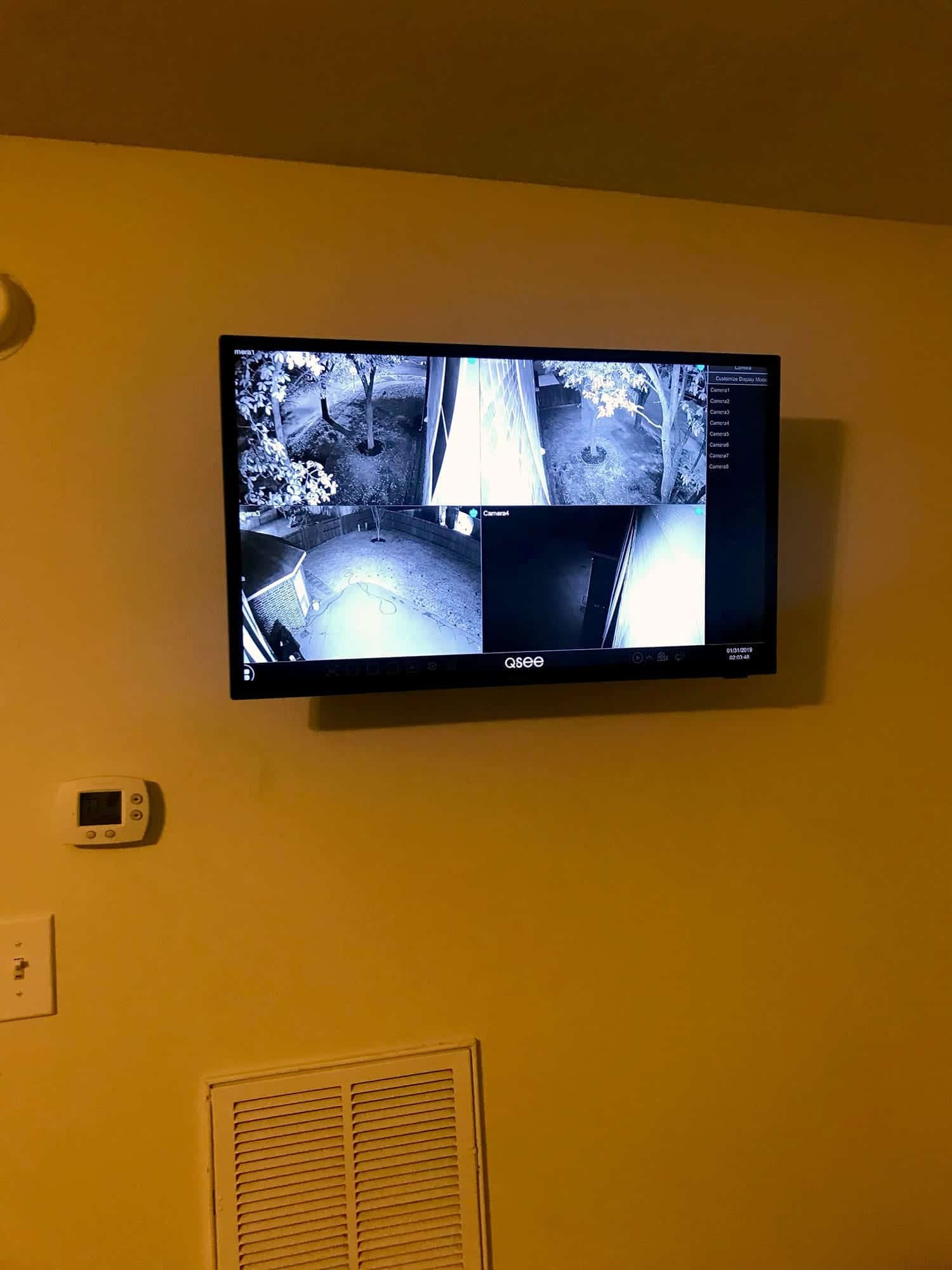 Wall-mounted four-camera security monitor showing night-vision yard and driveway footage