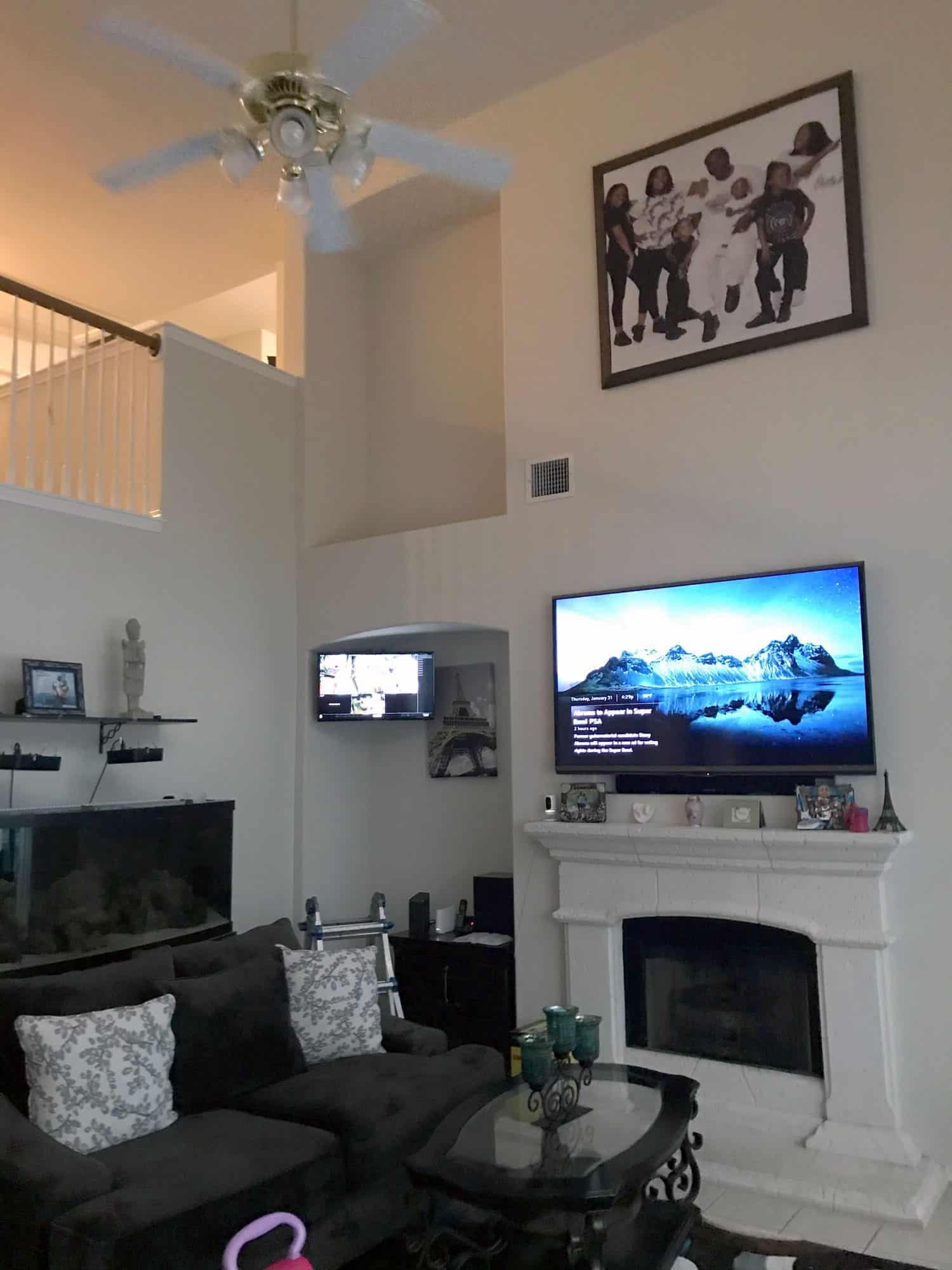 Two-story living room with a TV mounted above a white fireplace and a second smaller TV mounted in a side alcove