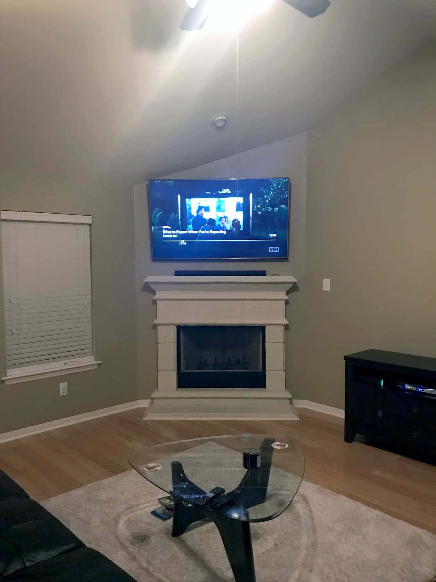 TV mounted above a white fireplace in a vaulted-ceiling living room, playing a VH1 program