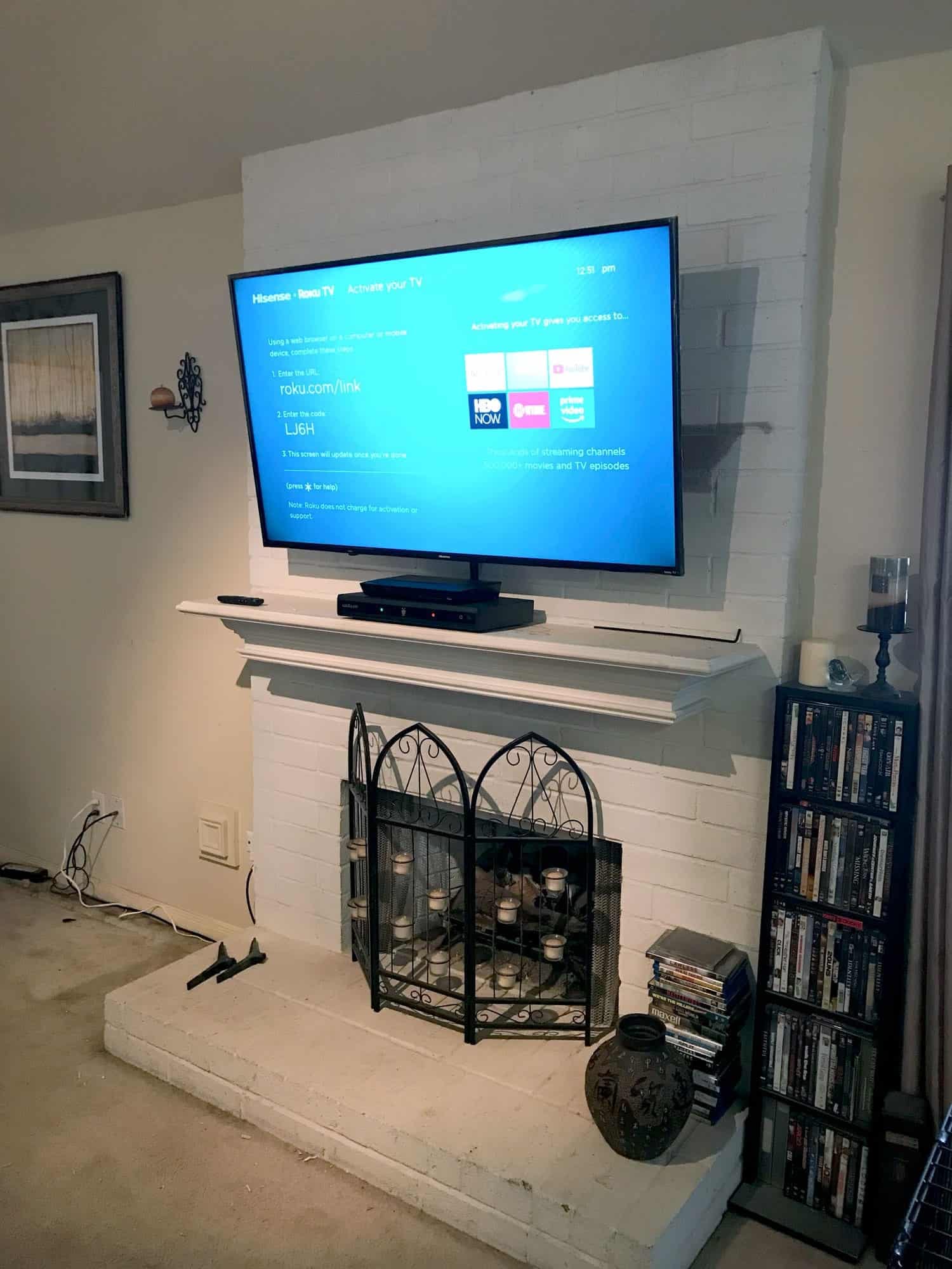 TV mounted above a white painted brick fireplace showing the Roku TV activation screen, next to a DVD collection