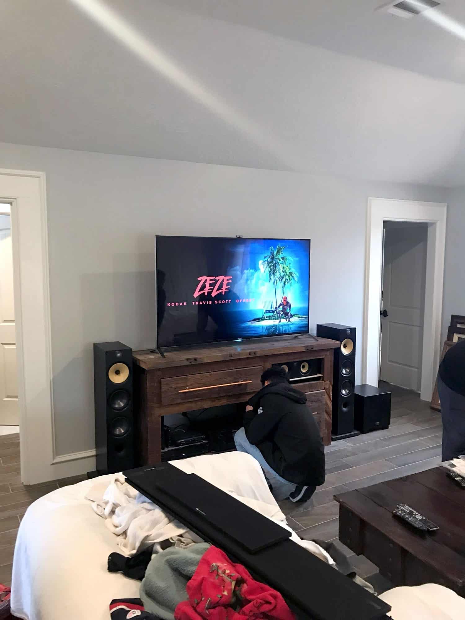 TV mounted on a wood console flanked by tall tower speakers, with an installer wiring equipment underneath