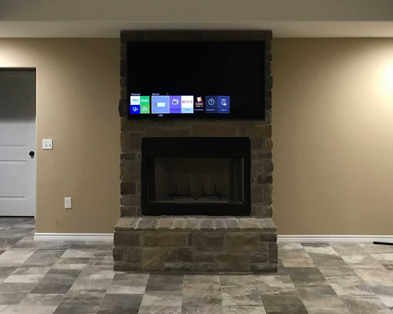 TV mounted above a stone fireplace showing the streaming apps menu in a basement media room