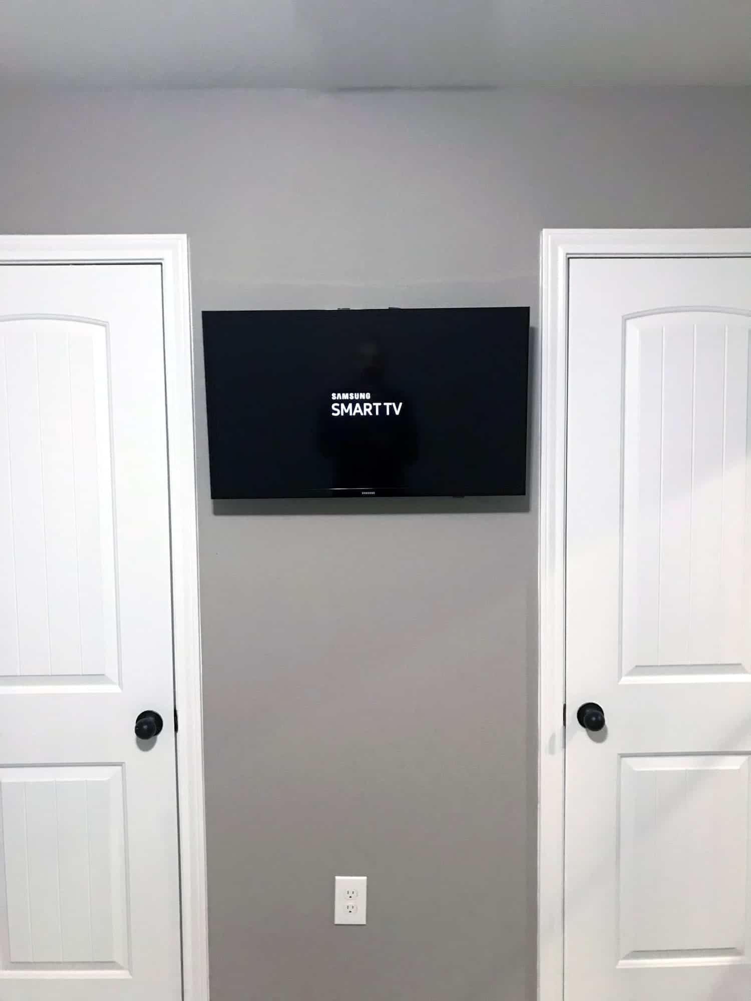 TV mounted on a wall between two closet doors displaying the Samsung Smart TV startup screen