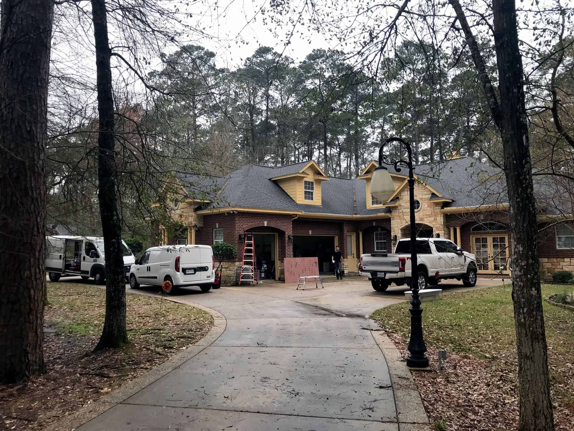 Exterior of a large brick and stone home with installation vans and a work truck parked in the driveway