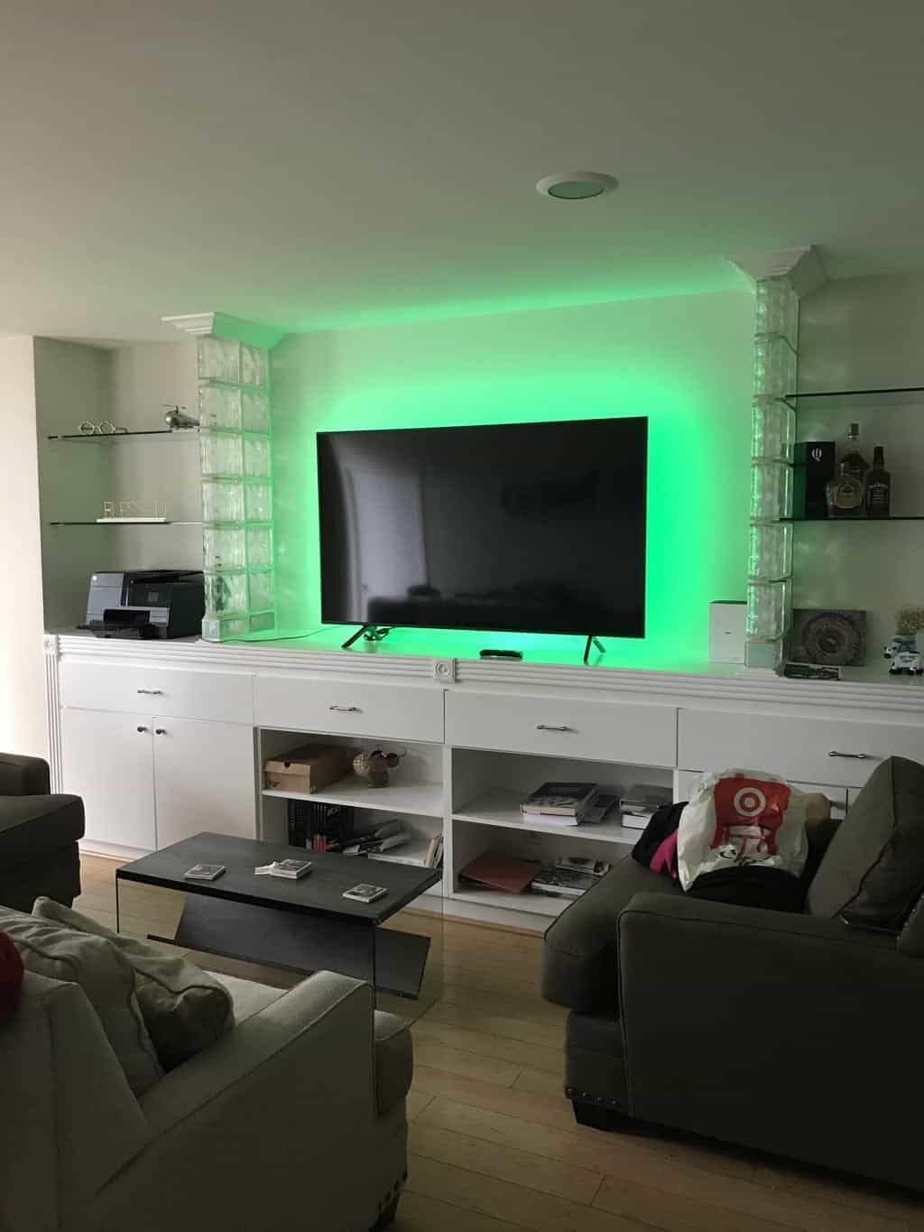 TV with green LED accent lighting mounted above white cabinetry between glass block columns